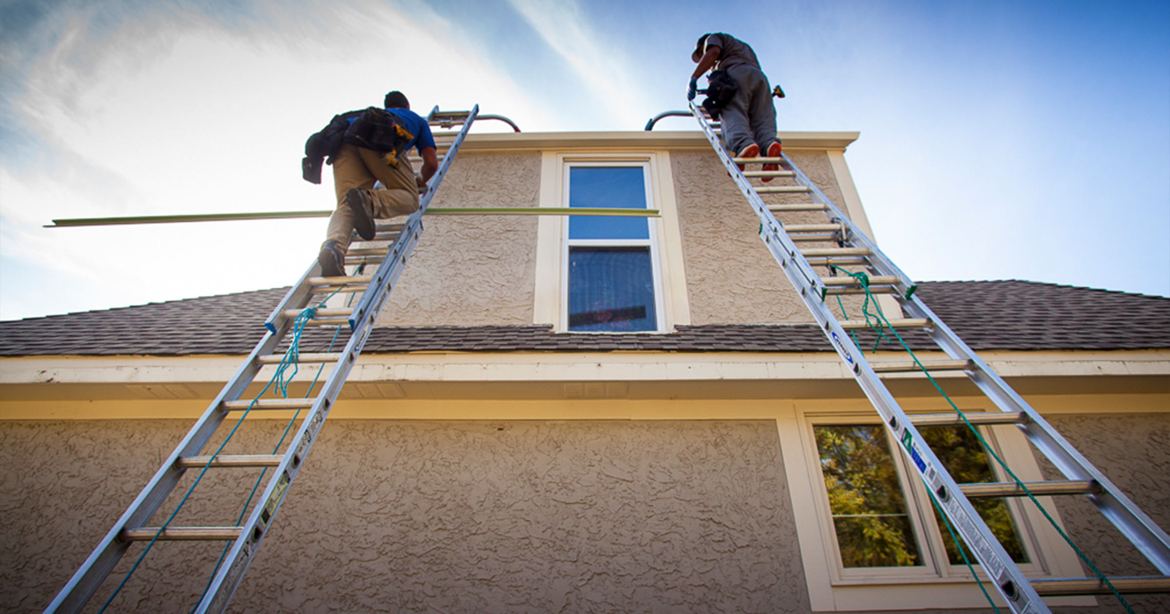 Two workers on ladders installing gutters on a house
